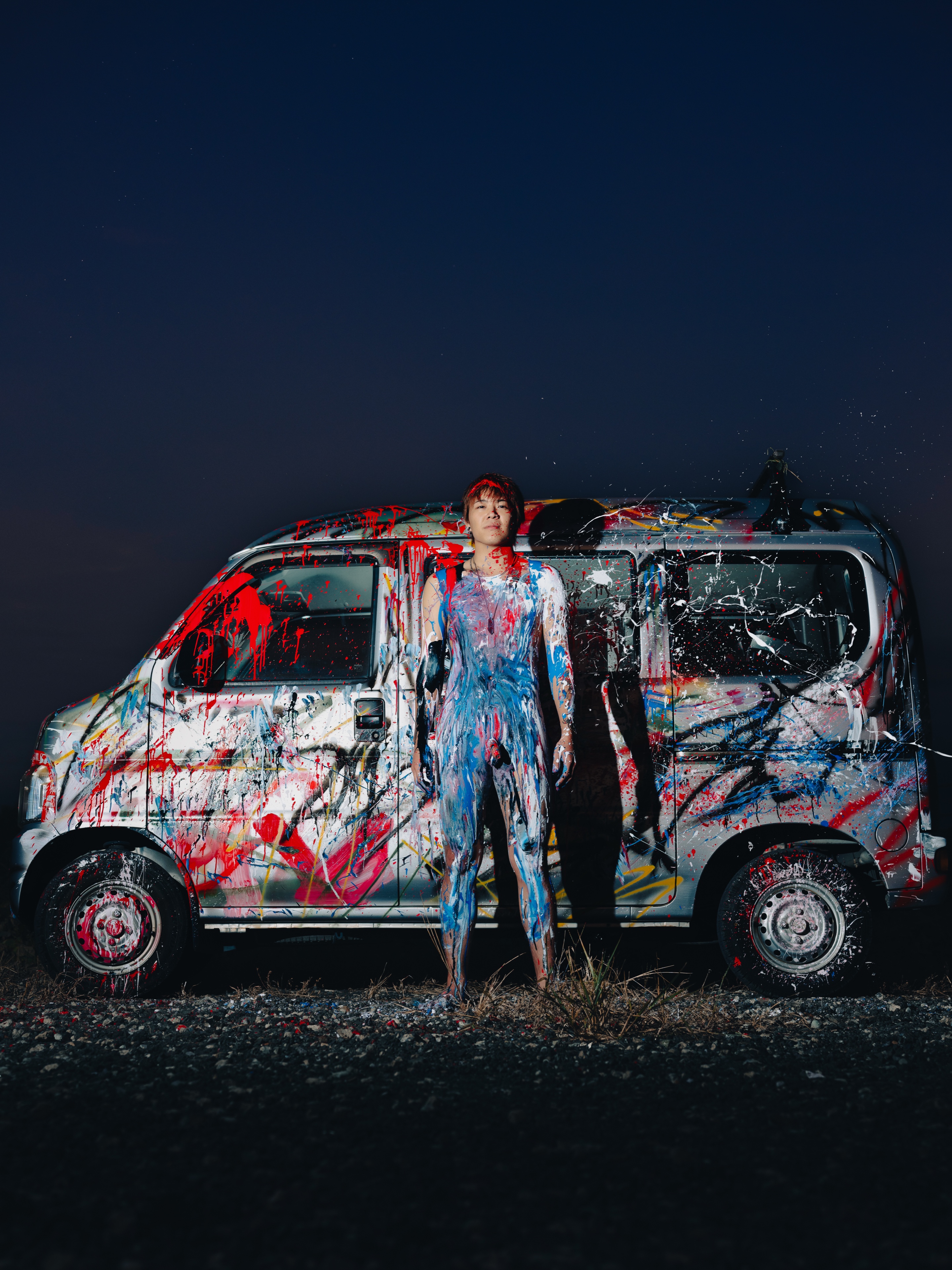 TAKAHASHI LAB ART — a person and a van covered in the same red and white pattern, outdoors at dusk