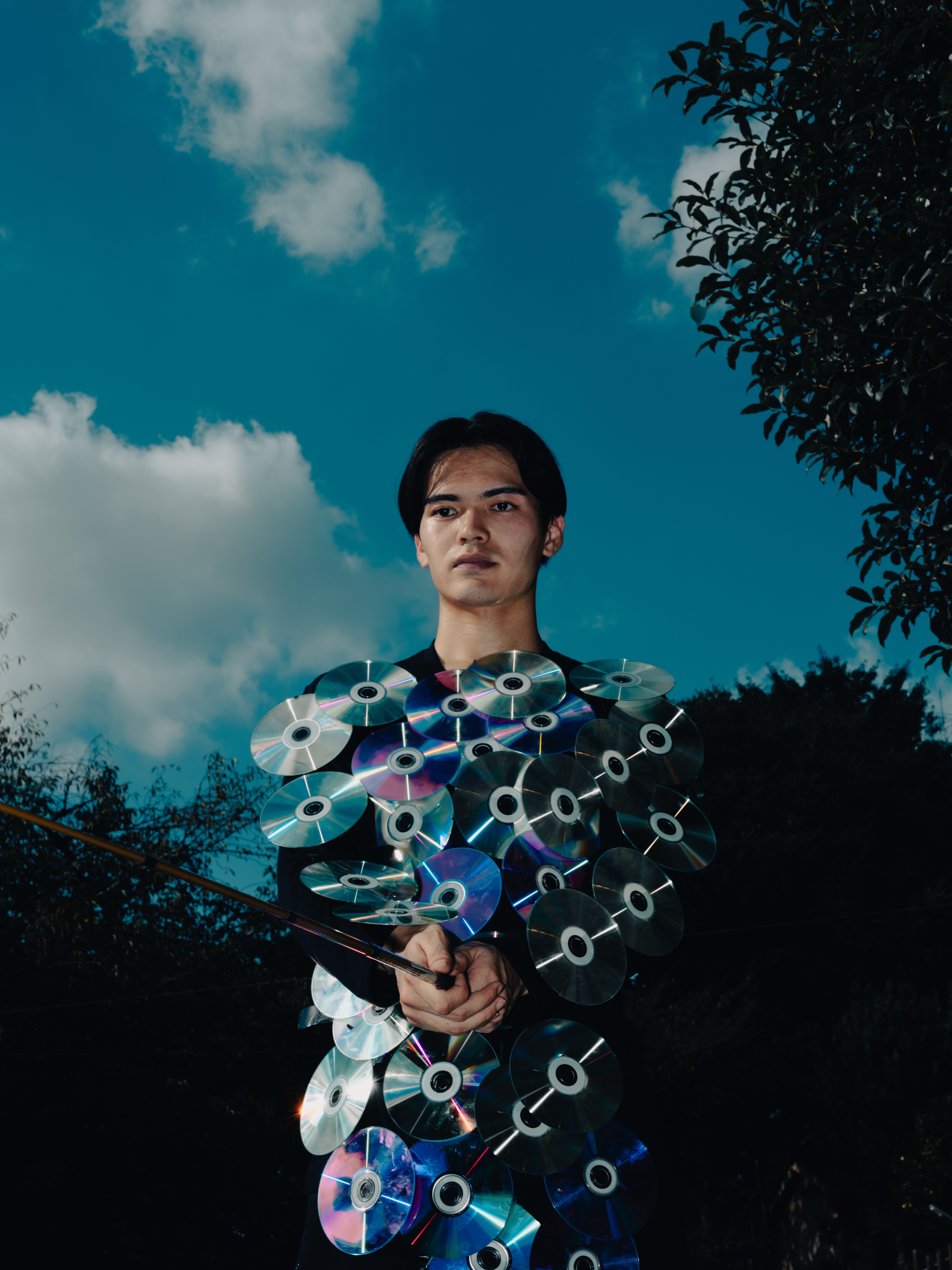 TAKAHASHI LAB ART — a person in a blue floral-patterned garment against a blue sky with clouds and green foliage