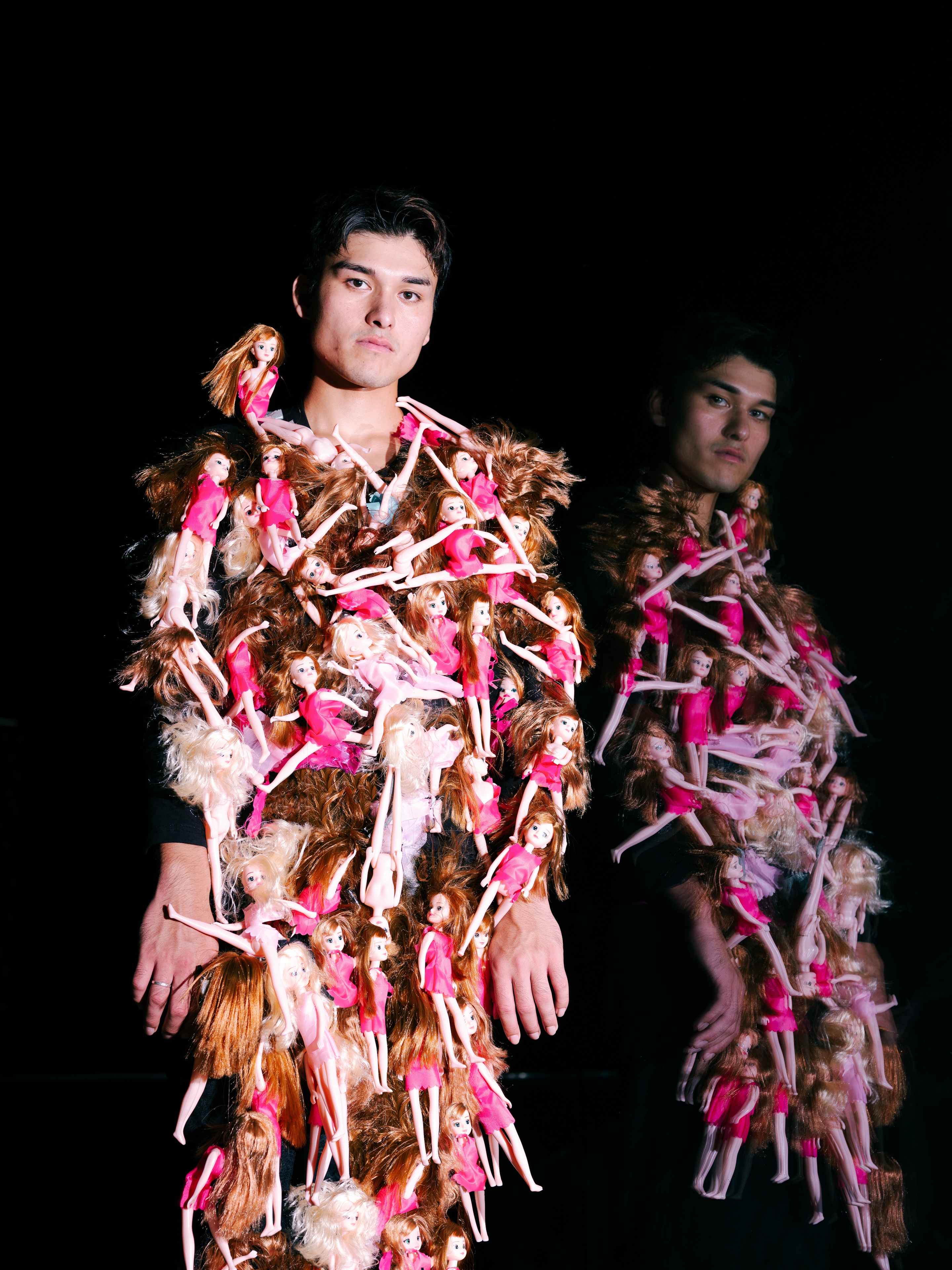 TAKAHASHI LAB ART — two people wearing garments made of pink and red strips of material, standing against a black background